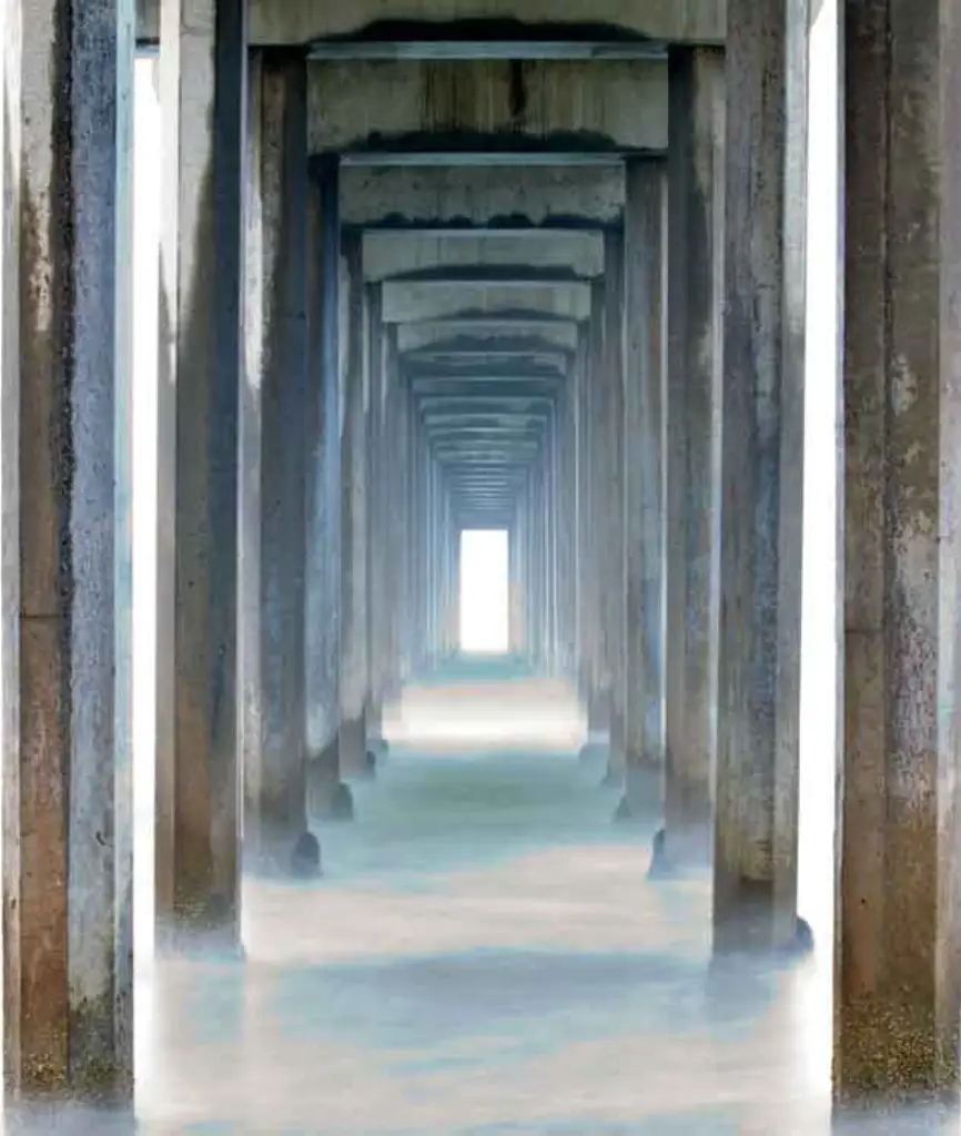 A tranquil view beneath a pier, featuring weathered concrete pillars extending into a misty, light-filled horizon over calm water